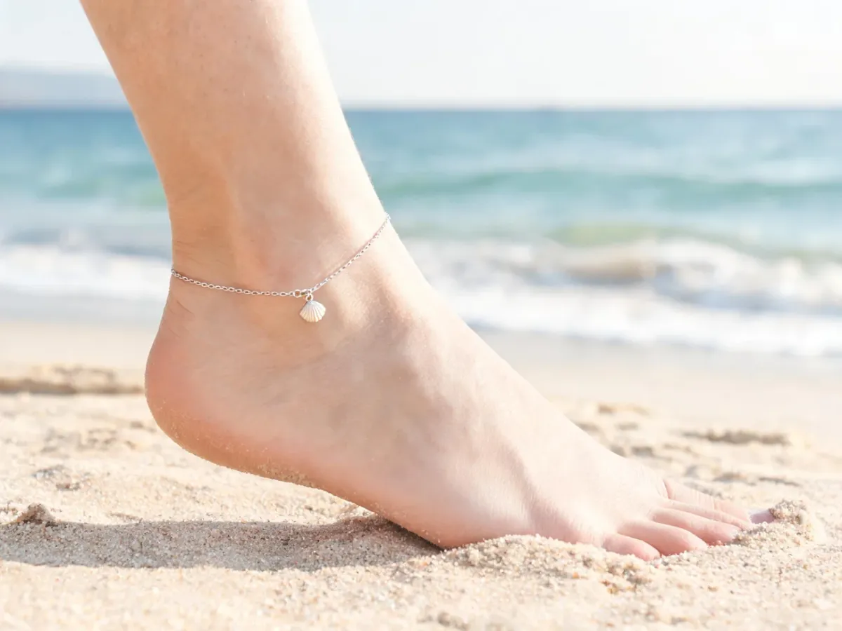 Kobieca kostka z delikatną srebrną bransoletką na plaży, symbol lekkości, wolności i letniego stylu życia.
